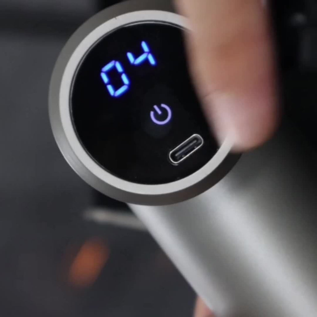 A close-up of the Handheld Massage Gun's display shows “04” in blue, a power button symbol, and a USB-C port. The ultra-compact massager is USB powered, with a finger touching its screen—ideal for deep tissue relief.